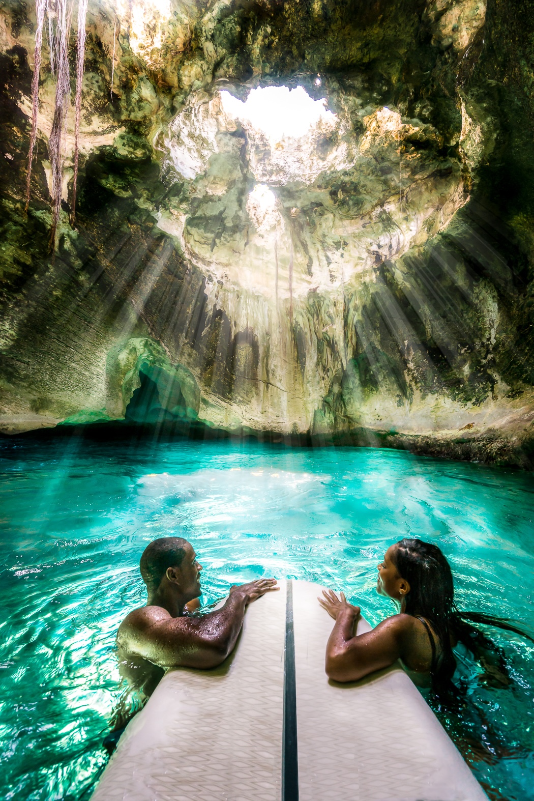 Dos figuras dentro de una gruta marina con luz entrando por una abertura en el techo