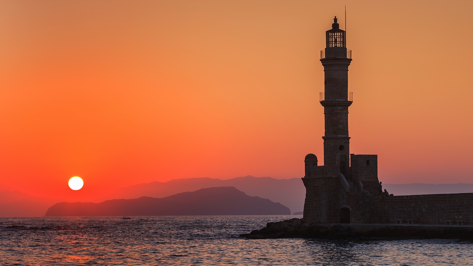 View of a harbor channel entrance with a small lighthouse at red sunset