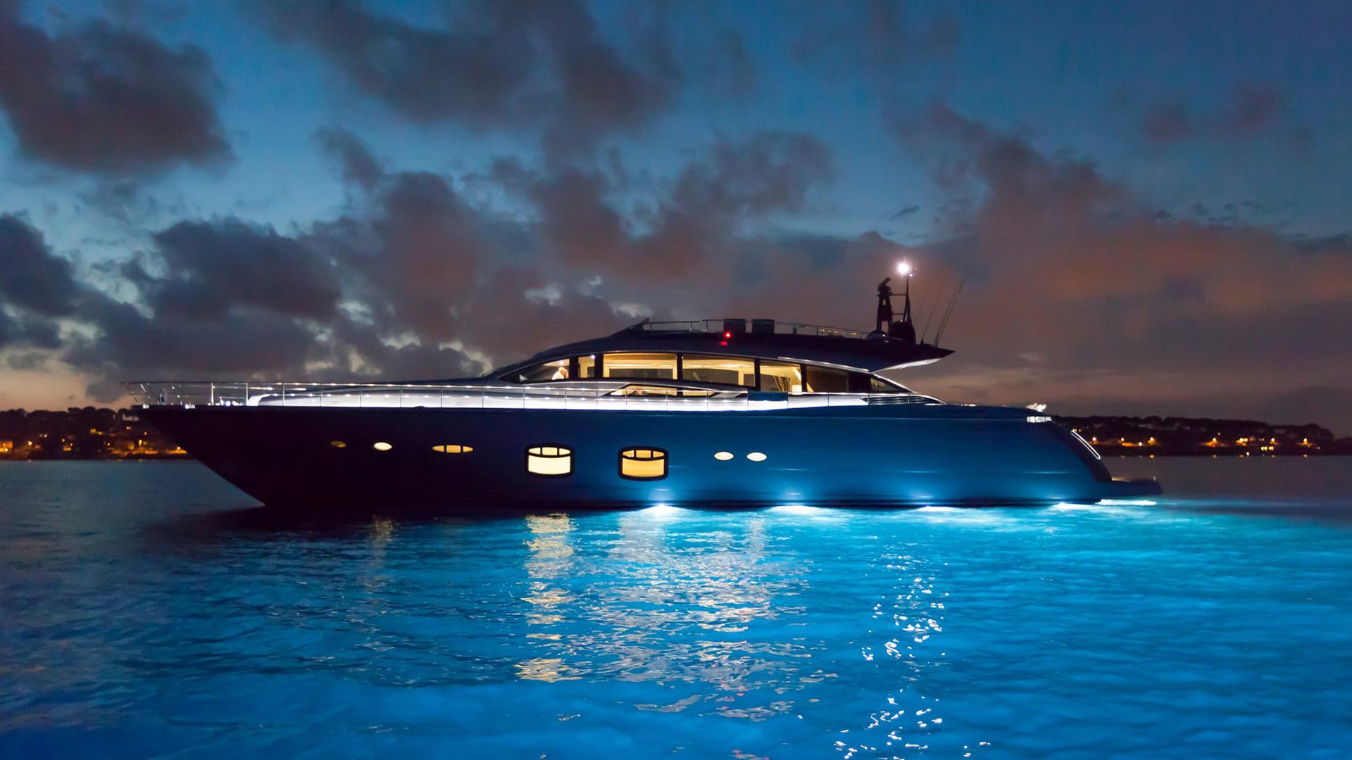 Profile view of a modern yacht at night with all underwater lights on