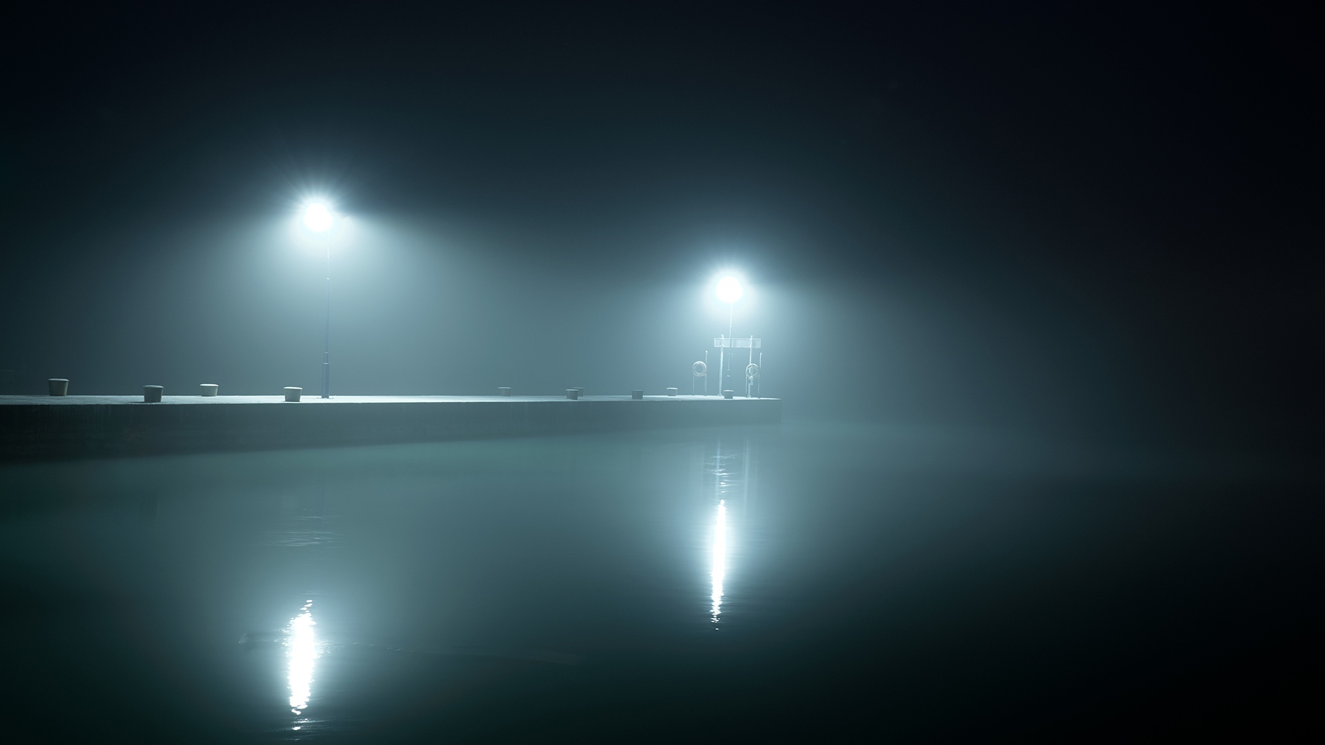View from the water of an empty pier with two white lights cutting through fog