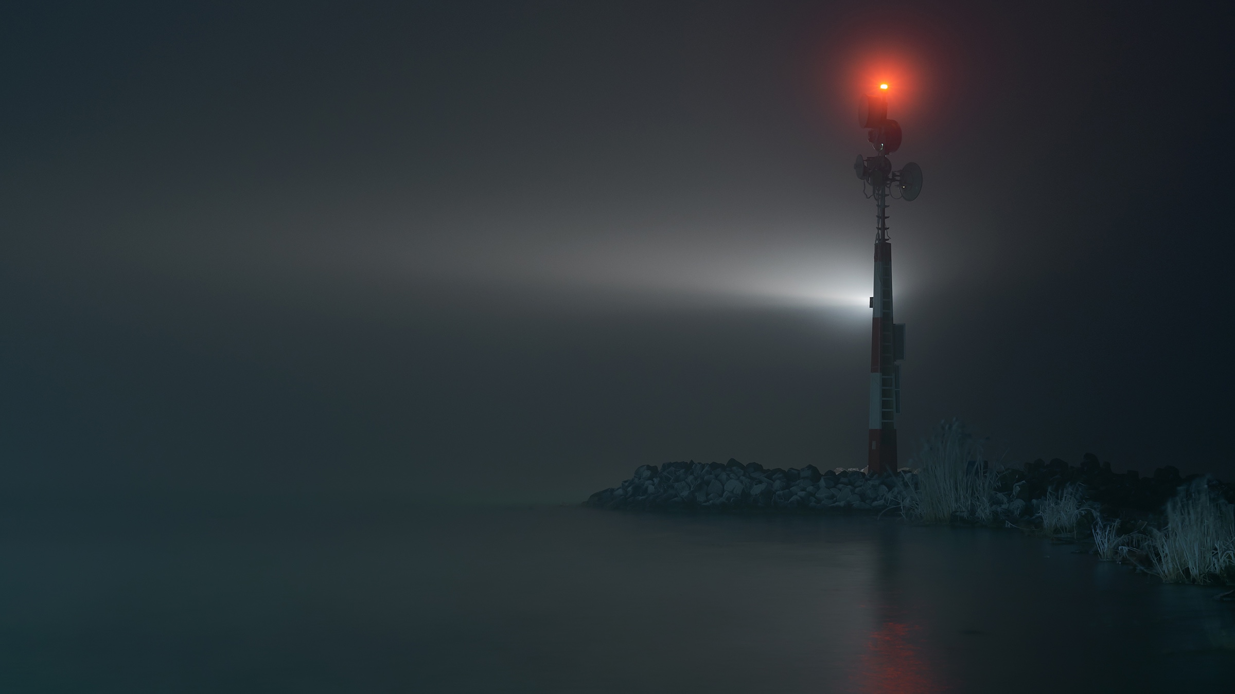 Small channel-entrance lighthouse at night with light fog, seen from the water