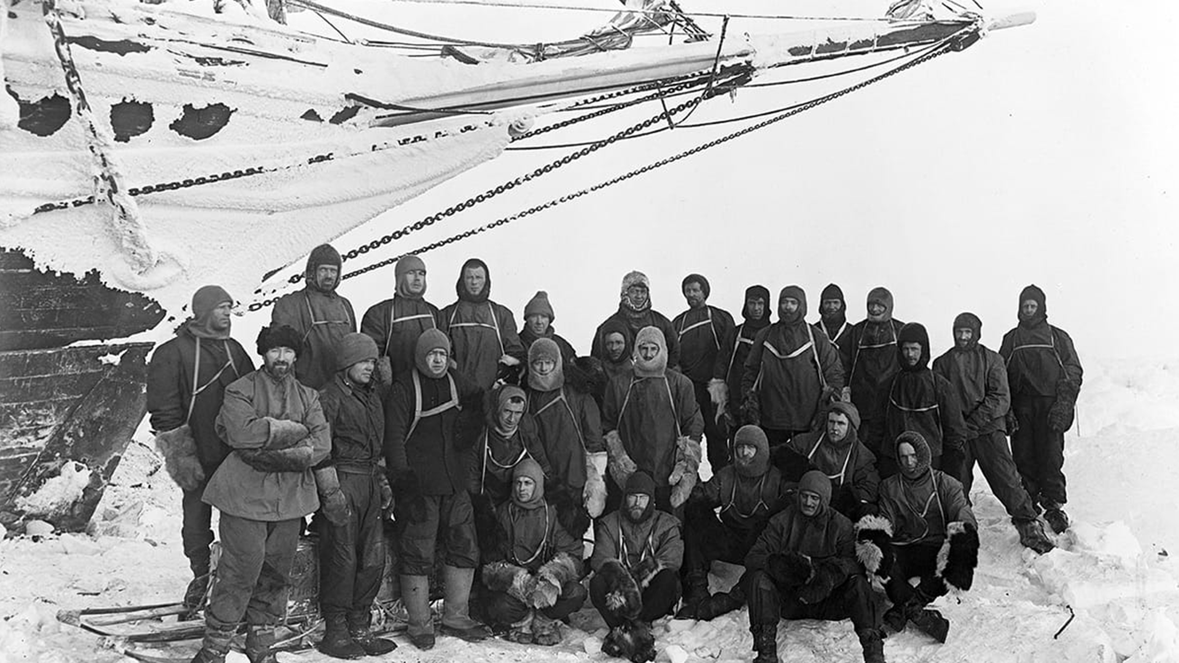 The crew of the Endurance gathered in full polar clothing beneath the bow of the ship, photographed by Frank Hurley