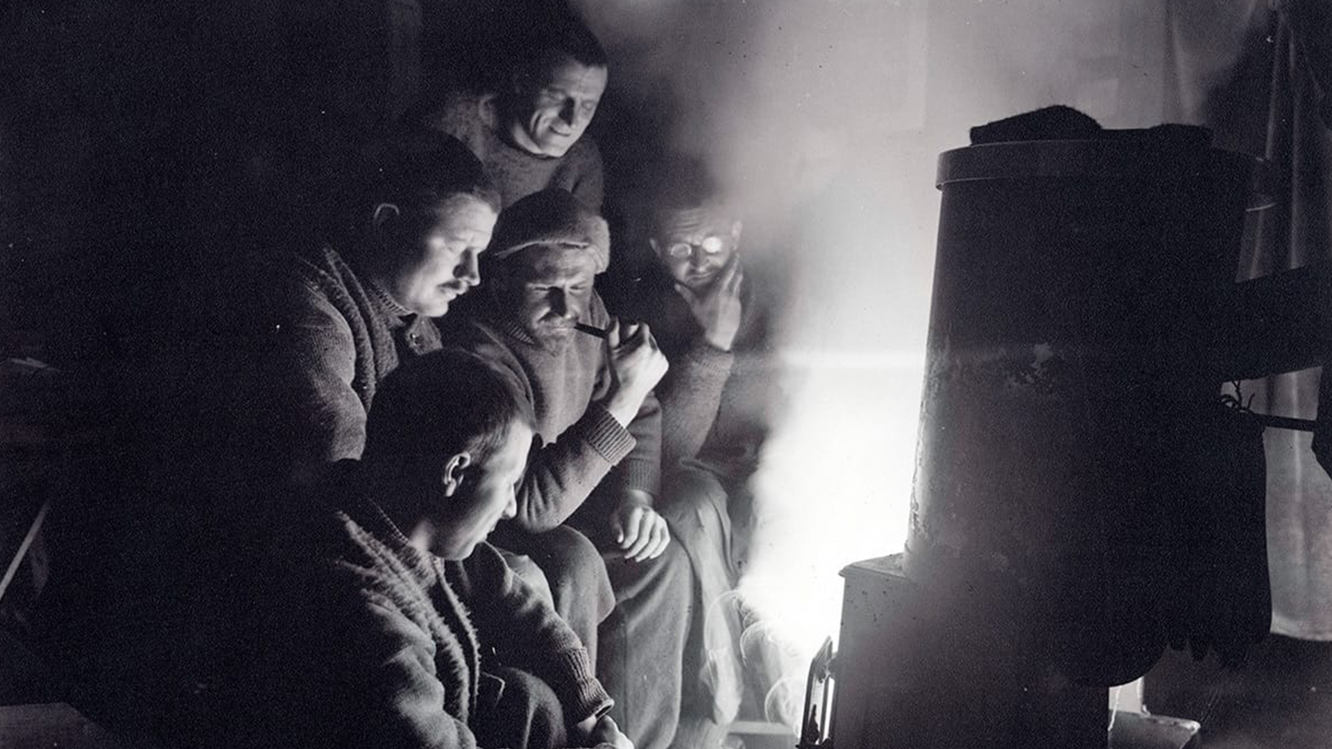 Group of crew members gathered around a stove in cold weather