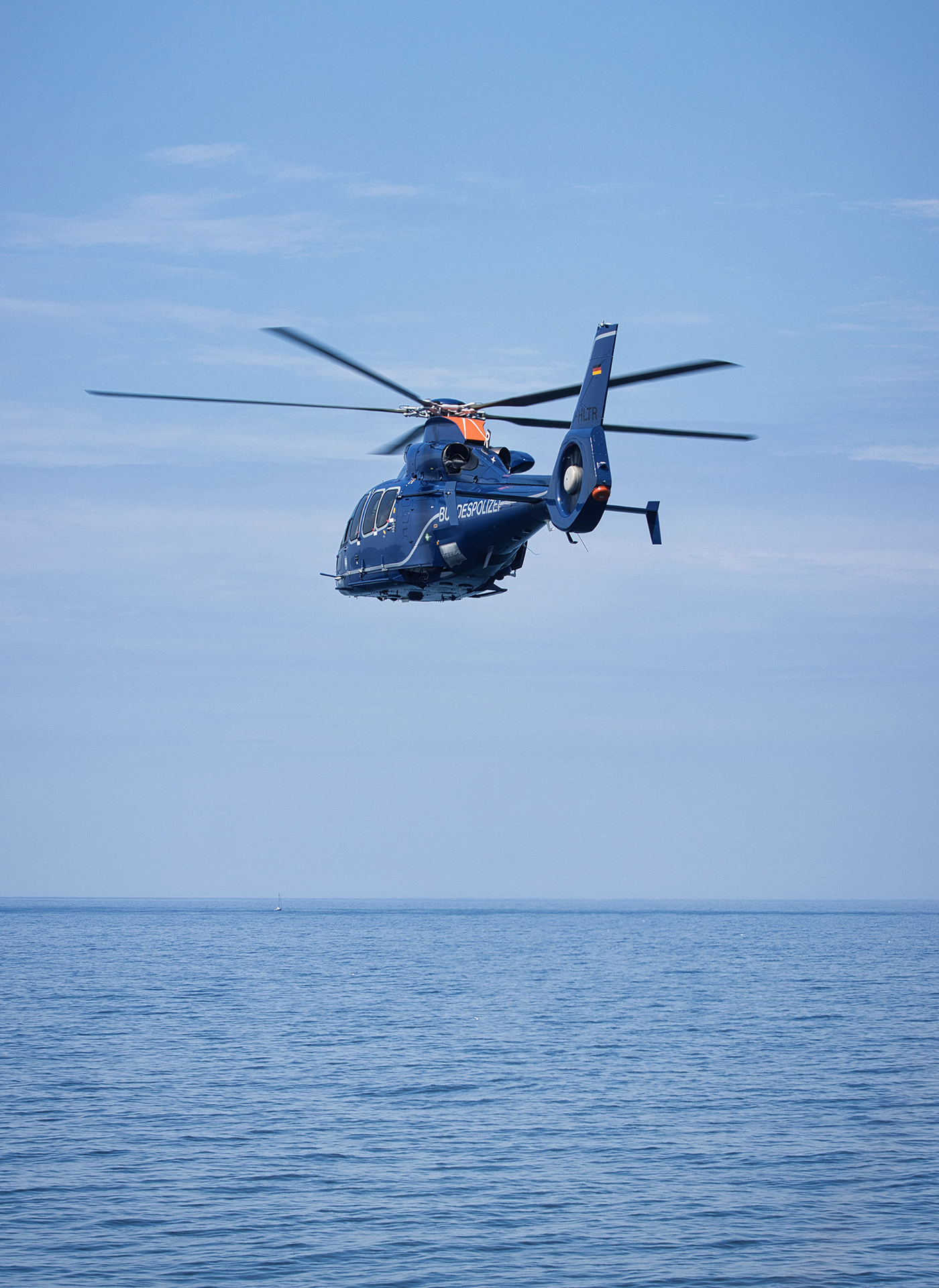 Modern helicopter seen in three-quarter rear profile, flying low over the water